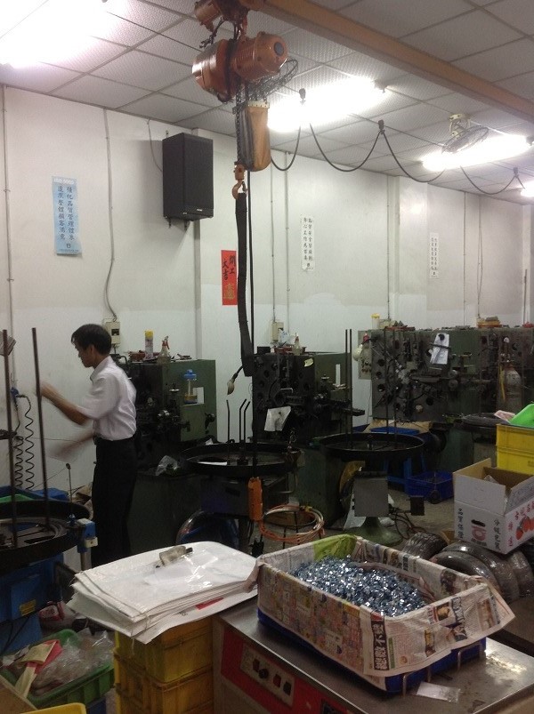 弘志工廠人員於加工機台旁作業，周圍設有線材供料架與零件容器
